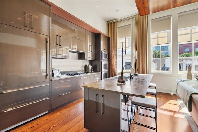 kitchen with sink, stainless steel appliances, an island with sink, a kitchen bar, and light wood-type flooring