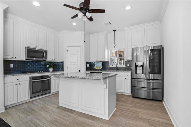 kitchen with hanging light fixtures, ornamental molding, appliances with stainless steel finishes, a kitchen island, and white cabinetry