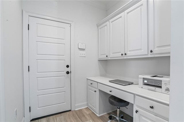 office area with built in desk, light wood-type flooring, and ornamental molding