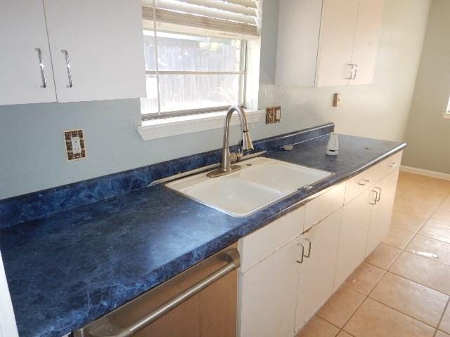 kitchen featuring white cabinets, stainless steel dishwasher, light tile patterned floors, and sink