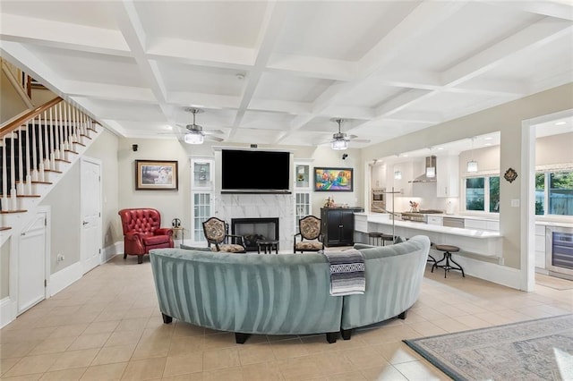 tiled living room with beam ceiling, ceiling fan, a high end fireplace, and coffered ceiling