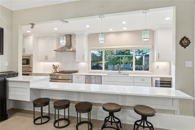 kitchen with decorative light fixtures, white cabinetry, stainless steel appliances, and wall chimney range hood