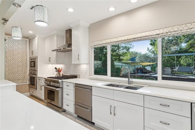 kitchen with pendant lighting, wall chimney range hood, sink, appliances with stainless steel finishes, and white cabinetry