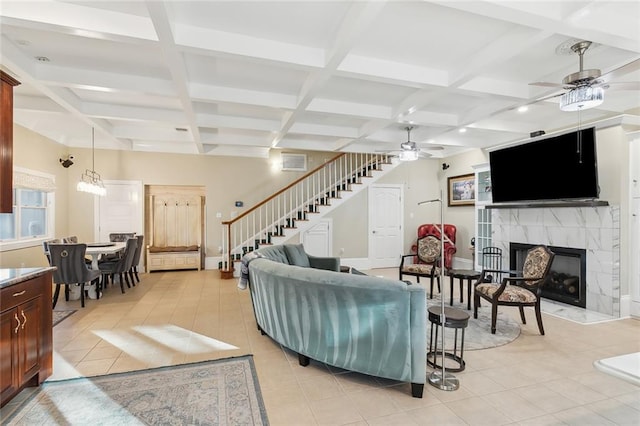 tiled living room featuring ceiling fan, beamed ceiling, a high end fireplace, and coffered ceiling