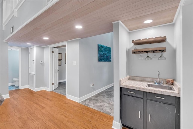 bar with light wood-type flooring, gray cabinets, wood ceiling, and sink