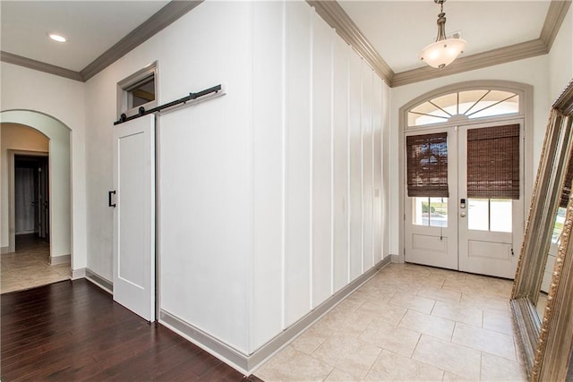 foyer entrance featuring a barn door, light wood-type flooring, ornamental molding, and french doors