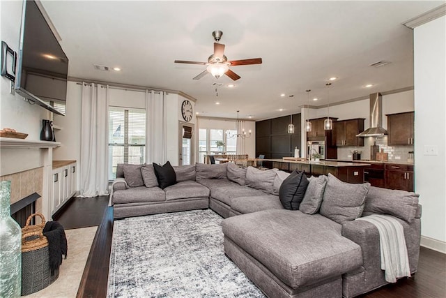 living room with ceiling fan with notable chandelier, dark hardwood / wood-style flooring, ornamental molding, and a tile fireplace