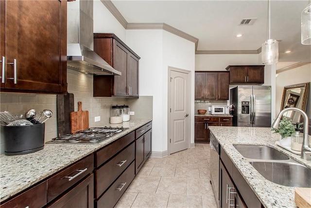 kitchen with appliances with stainless steel finishes, light stone counters, sink, wall chimney range hood, and hanging light fixtures