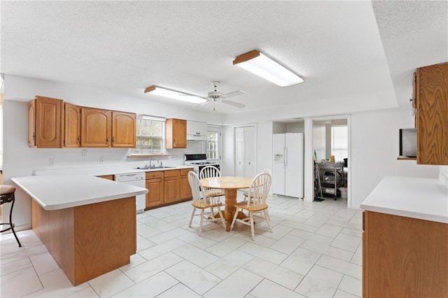 kitchen with a peninsula, white appliances, a sink, light countertops, and brown cabinetry