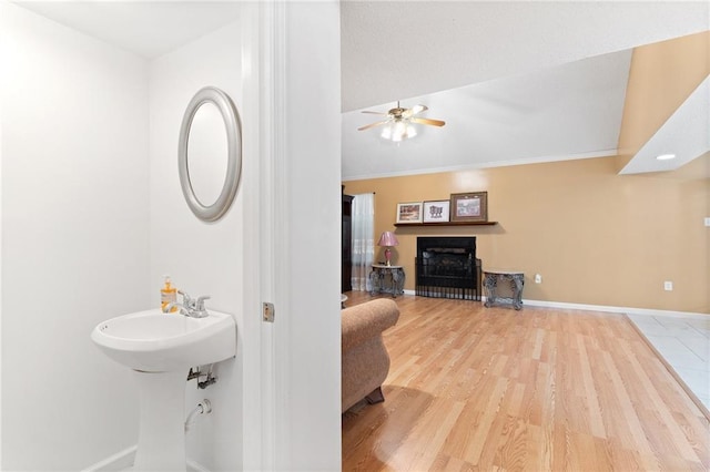 bathroom featuring a fireplace, ornamental molding, ceiling fan, wood finished floors, and baseboards