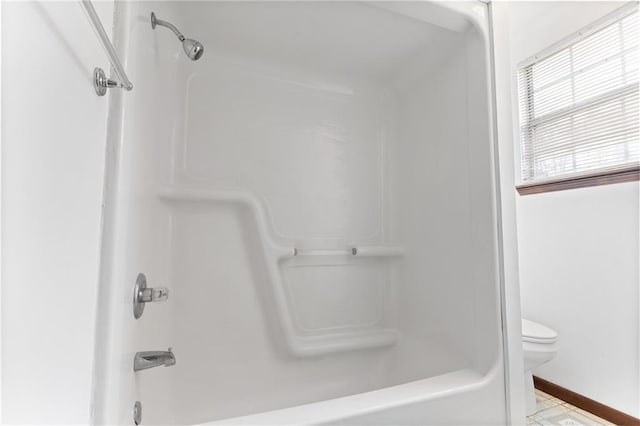 bathroom featuring washtub / shower combination, toilet, and baseboards