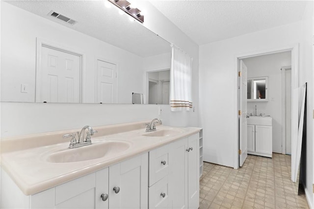 full bathroom featuring double vanity, a textured ceiling, visible vents, and a sink