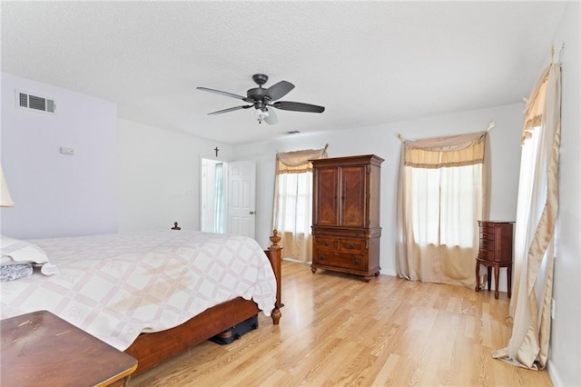 bedroom featuring light wood finished floors, multiple windows, visible vents, and a ceiling fan