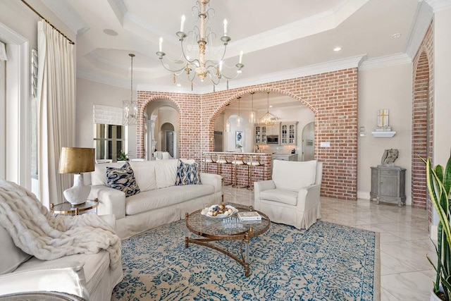 living room with a chandelier, a raised ceiling, ornamental molding, and brick wall