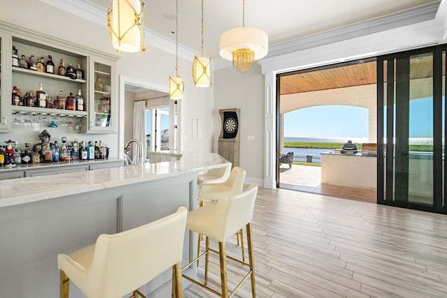 bar with light stone counters, plenty of natural light, decorative light fixtures, and light wood-type flooring