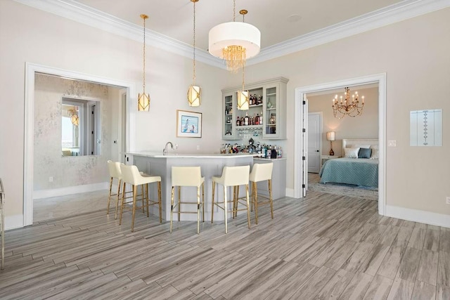 kitchen featuring ornamental molding, light hardwood / wood-style floors, white cabinetry, hanging light fixtures, and a breakfast bar area