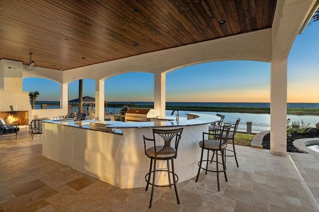 patio terrace at dusk featuring a water view, an outdoor bar, and a fireplace