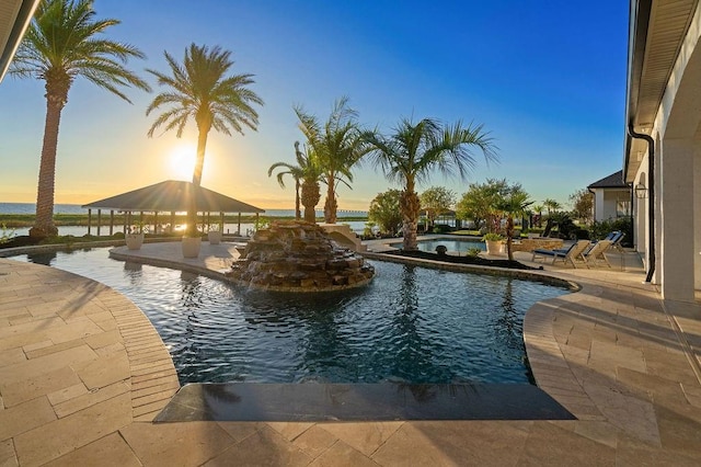 pool at dusk featuring a gazebo, a water view, and a patio area