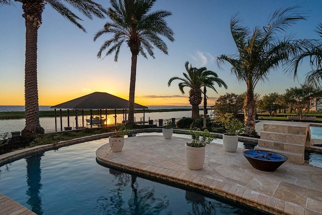 pool at dusk with a gazebo, a patio area, and a water view