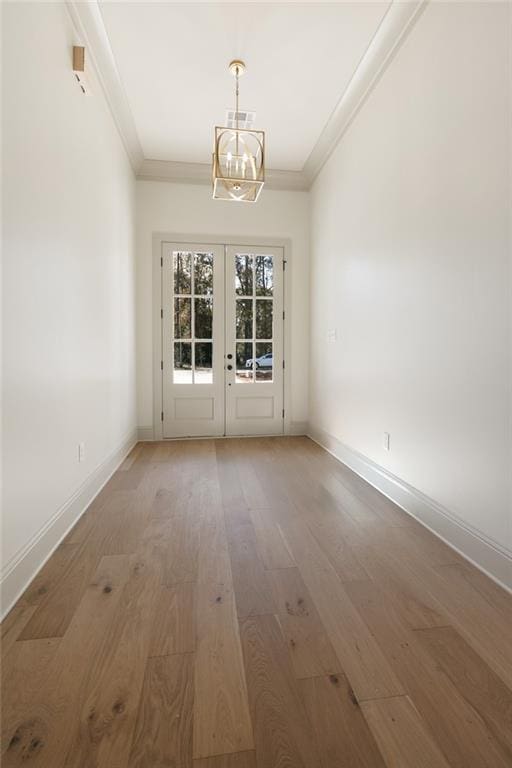 spare room with a chandelier, wood-type flooring, ornamental molding, and french doors