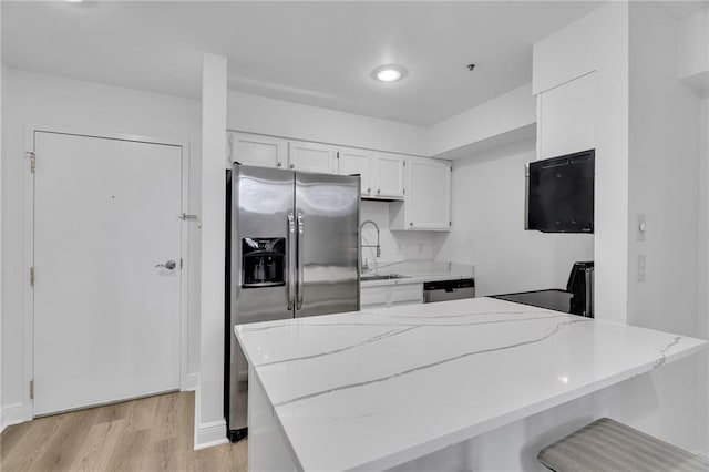 kitchen featuring light stone countertops, light wood-type flooring, stainless steel appliances, sink, and white cabinetry