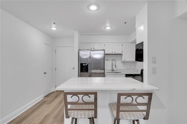 kitchen with white cabinets, a kitchen breakfast bar, sink, stainless steel fridge, and light wood-type flooring