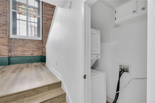 clothes washing area featuring hardwood / wood-style floors, stacked washer and dryer, and brick wall