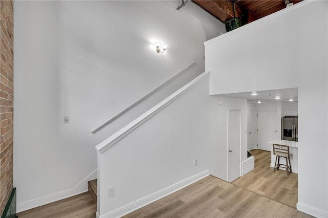 unfurnished living room with brick wall, a high ceiling, and light hardwood / wood-style floors