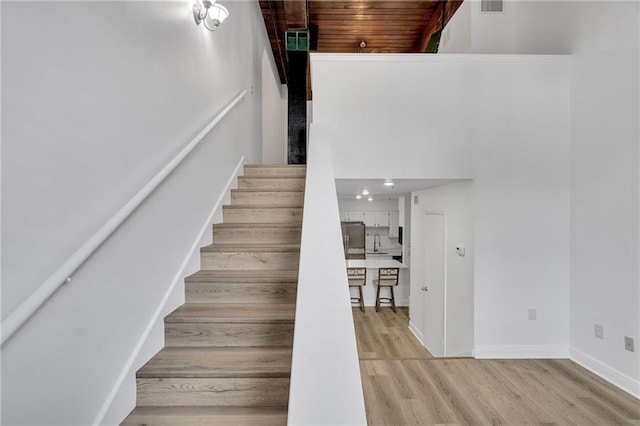 stairway featuring wood-type flooring, a towering ceiling, and wood ceiling