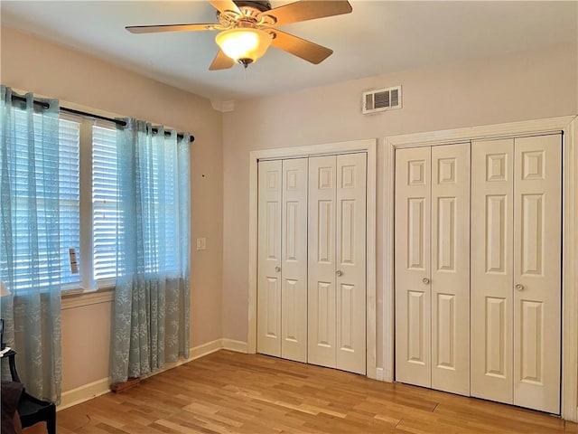 unfurnished bedroom with two closets, ceiling fan, and light wood-type flooring