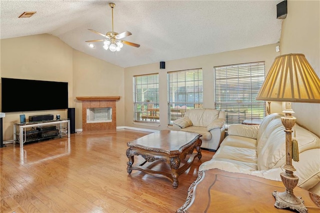 living room featuring ceiling fan, a textured ceiling, vaulted ceiling, a fireplace, and light wood-type flooring