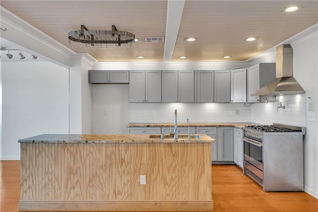 kitchen with light wood-type flooring, light stone counters, wall chimney exhaust hood, sink, and stainless steel range with gas stovetop