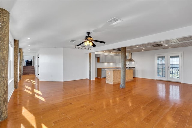 unfurnished living room with ceiling fan, french doors, and light hardwood / wood-style flooring