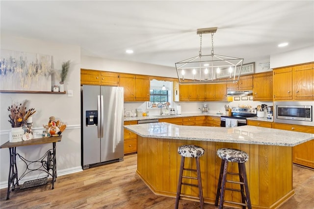 kitchen featuring a center island, hanging light fixtures, light stone counters, light hardwood / wood-style floors, and appliances with stainless steel finishes