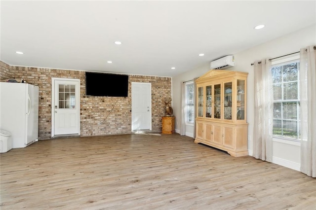 unfurnished room with brick wall, a wall mounted air conditioner, and light wood-type flooring