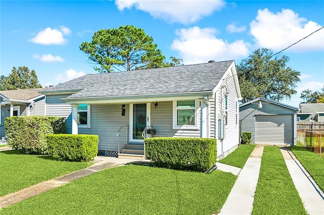 bungalow featuring covered porch, a garage, a front lawn, and an outdoor structure