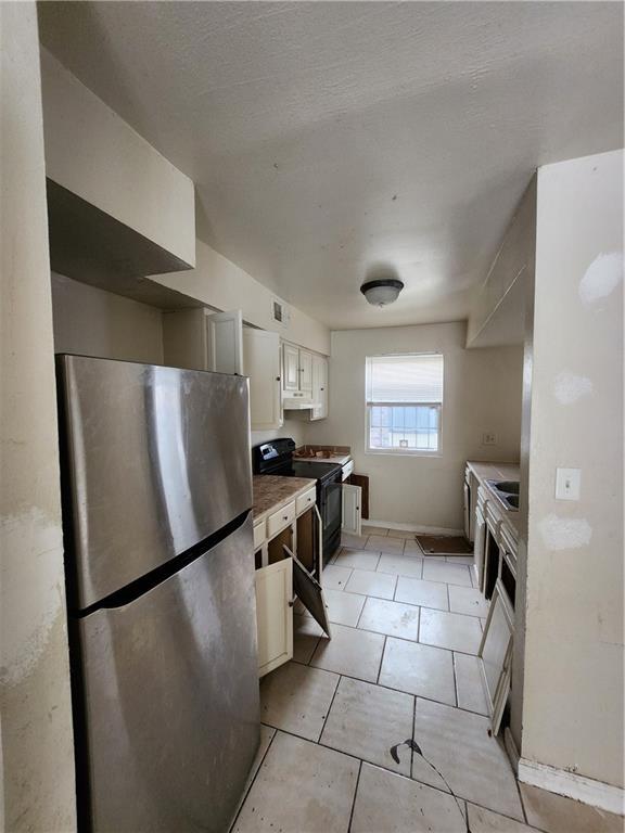 kitchen featuring extractor fan, white cabinetry, light tile patterned floors, black / electric stove, and stainless steel fridge