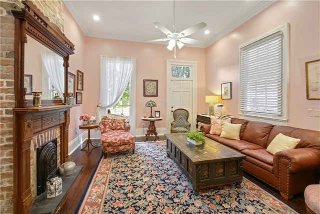 living room featuring wood-type flooring, a brick fireplace, ceiling fan, and ornamental molding