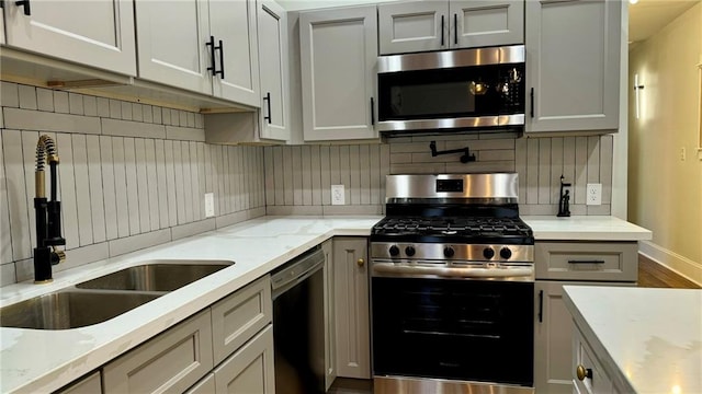 kitchen featuring backsplash, stainless steel appliances, gray cabinetry, and sink