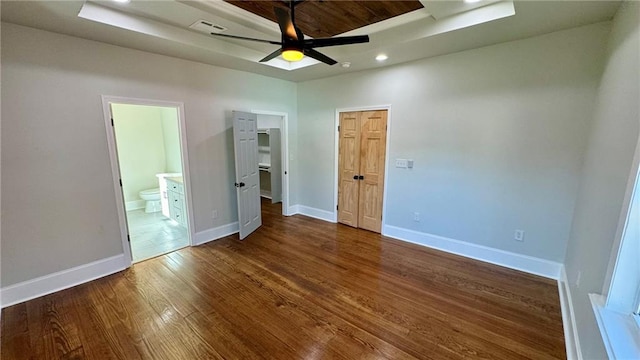 unfurnished bedroom featuring connected bathroom, a tray ceiling, ceiling fan, and dark wood-type flooring