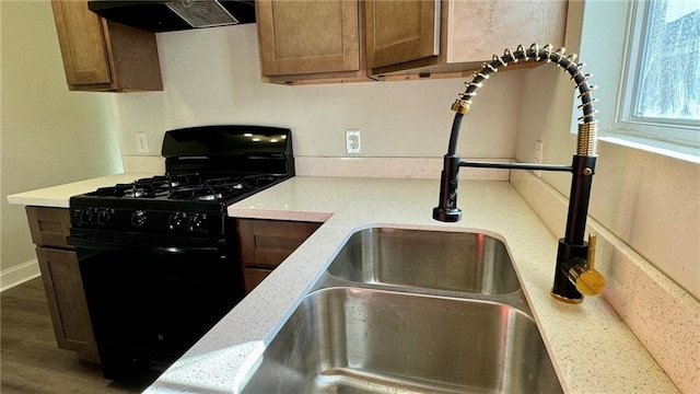 kitchen featuring light stone countertops, ventilation hood, dark wood-type flooring, sink, and black gas stove