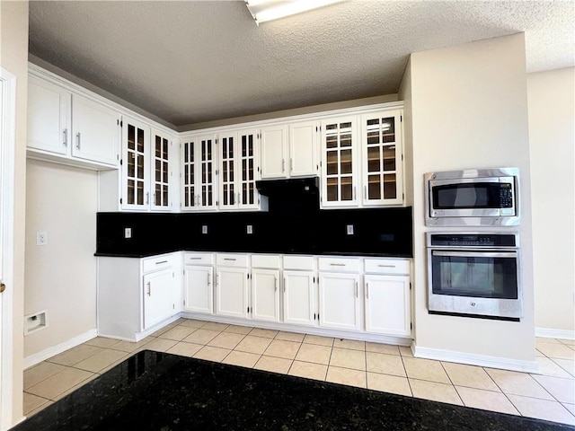 kitchen featuring dark countertops, light tile patterned floors, white cabinetry, and stainless steel appliances