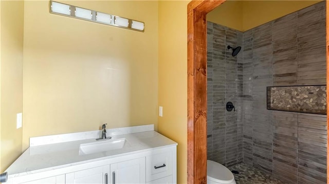 bathroom with tiled shower, vanity, and toilet