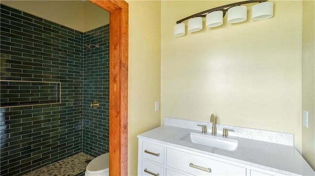 bathroom with a tile shower, vanity, and toilet