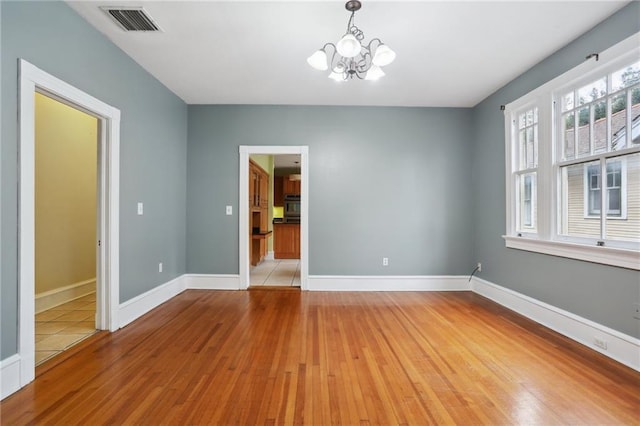 empty room featuring a chandelier and light hardwood / wood-style floors