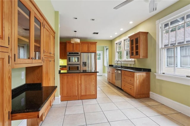 2808 Octavia St, New Orleans, LA 70115 - kitchen with stainless steel appliances, light tile patterned floors, glass insert cabinets, brown cabinetry, and hanging light fixtures