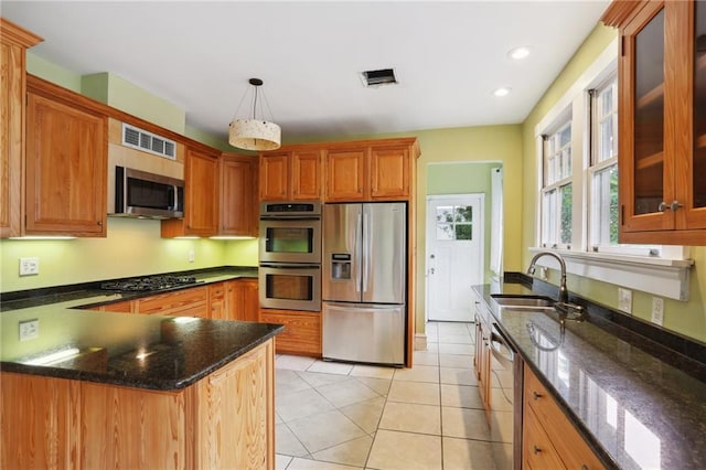 kitchen with appliances with stainless steel finishes, sink, pendant lighting, dark stone countertops, and light tile patterned flooring