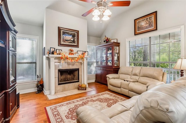 living room featuring vaulted ceiling, a tile fireplace, a wealth of natural light, and light hardwood / wood-style flooring