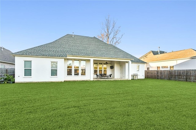 rear view of property featuring a yard, a patio, a shingled roof, ceiling fan, and a fenced backyard