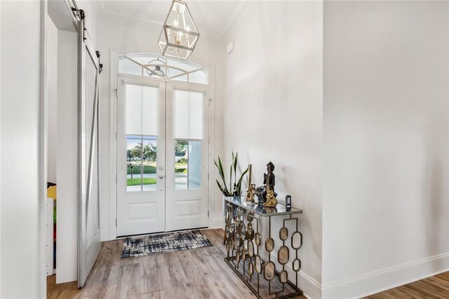 foyer entrance with baseboards, a barn door, ornamental molding, and wood finished floors